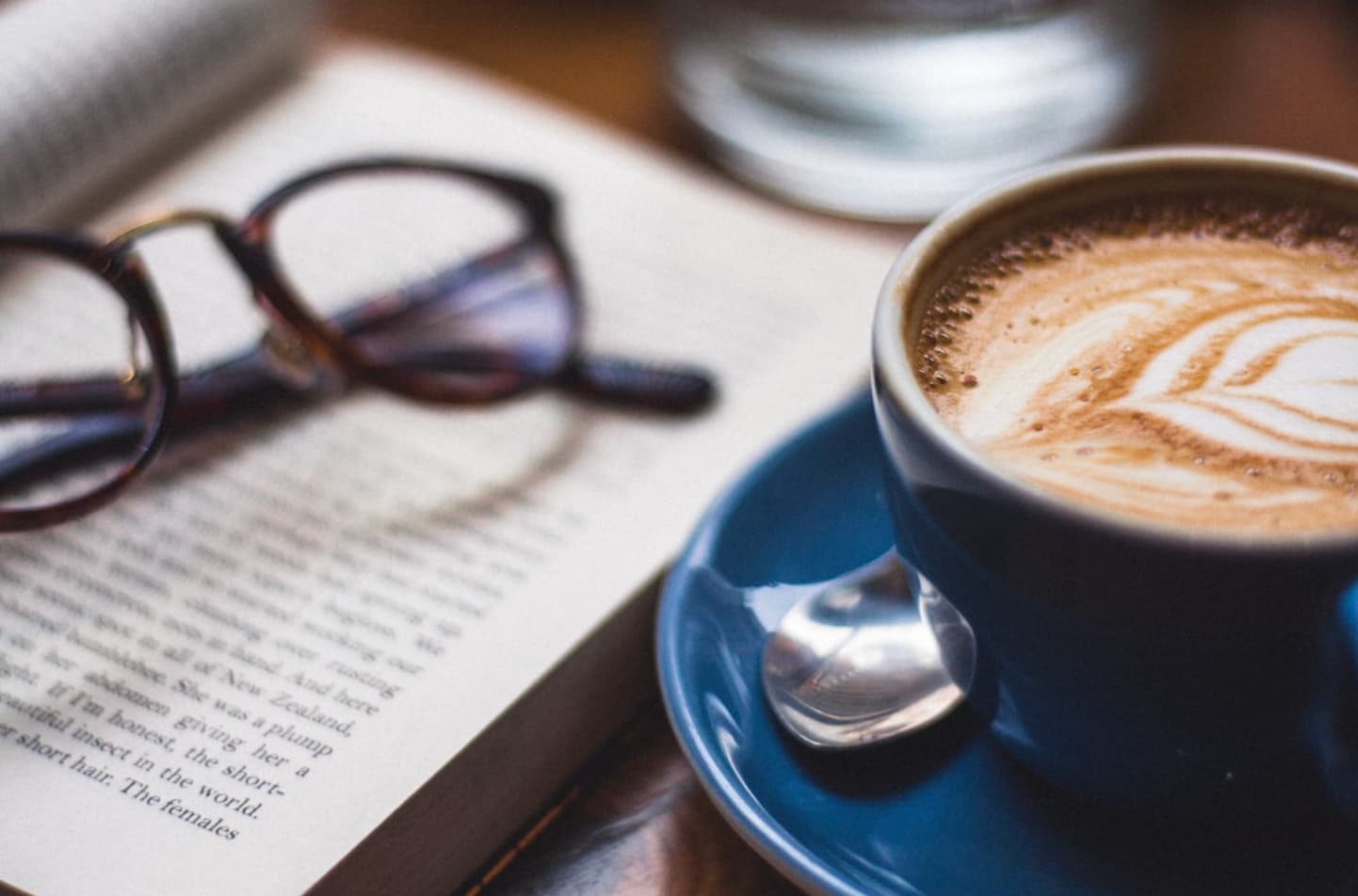 A cappuccino next to a book with glasses on top